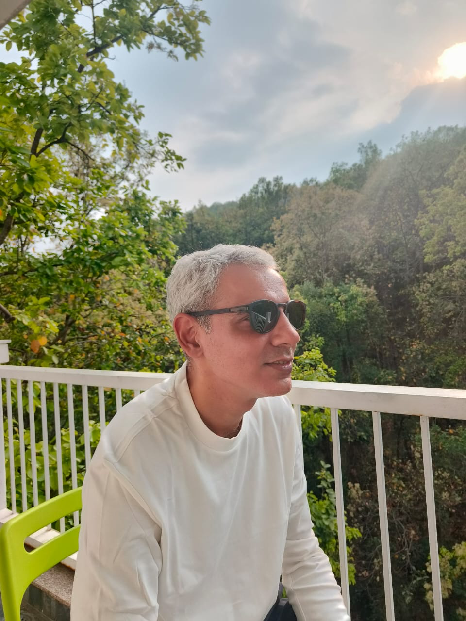 Man wearing sunglasses sitting on a balcony with greenery in the background